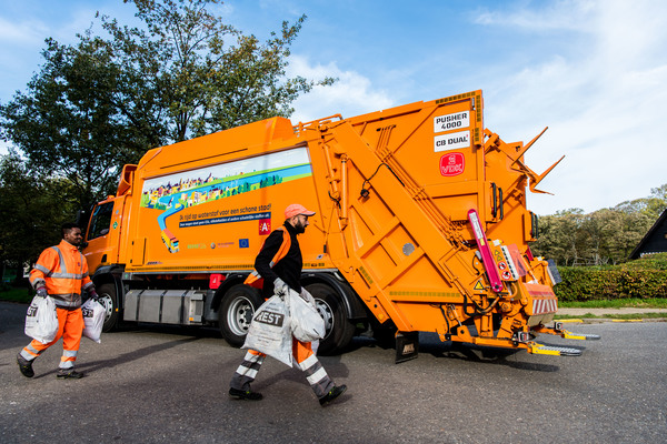 Stadsmedewerkers gooien restafvalzakken in de vuilniswagen.